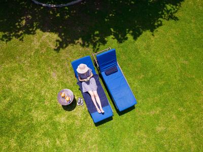 Person entspannt auf einer Liege im Garten neben einem Tisch mit Getränken.