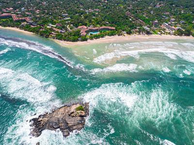 Luftaufnahme einer Küste mit grünen Wäldern, Sandstrand und blau-grünem, welligem Meer.