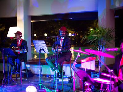 Drei Musiker spielen bei einer nächtlichen Veranstaltung in einem Hotel mit farbiger Beleuchtung.