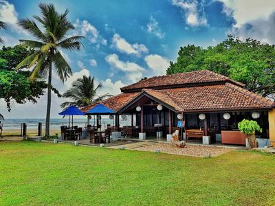 Strandhotel mit Terrasse, Sonnenschirmen und Palmen unter blauem Himmel.