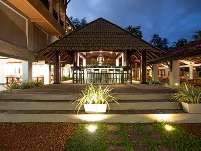 Beleuchteter Hotel-Eingang mit Treppen und tropischem Pavillon bei Nacht.