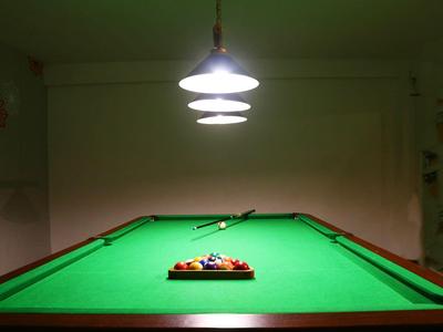 Ein beleuchteter Billardtisch mit aufgereihten bunten Kugeln in einem dunklen Raum.