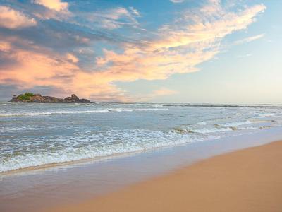 Sandstrand mit sanften Wellen, weiter Horizont und bunter Himmel mit Wolken bei Sonnenuntergang.