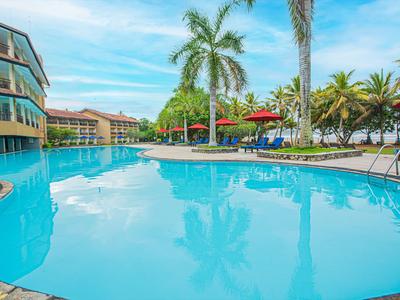 Großer Pool mit blauer Wasseroberfläche, umgeben von Hotelgebäuden und tropischen Palmen.