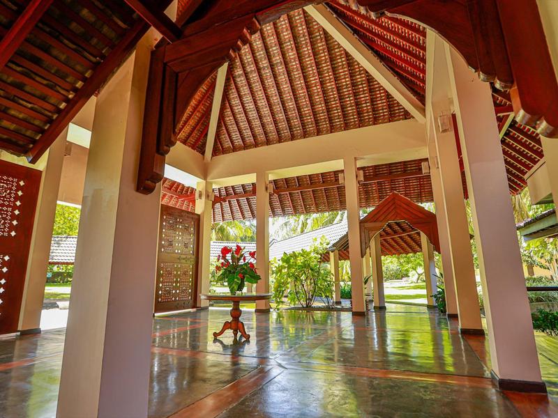 Offener Pavillon mit Holzsäulen, glänzendem Boden und tropischer Außenlandschaft bei Tageslicht.