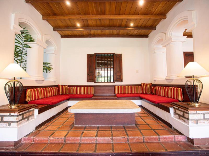 Helles Wohnzimmer mit roten Polstern, Holzbalkendecke und Terrakottaboden. Große Eckcouch mit Kissen.