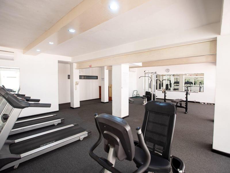 Heller Fitnessraum mit Laufbändern, Rudergerät und großen Spiegeln an der Wand.