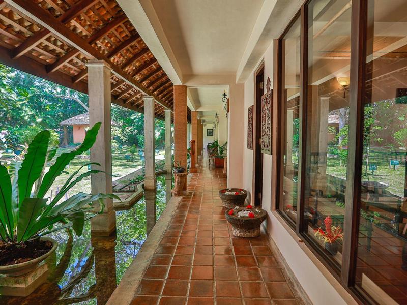 Langer überdachter Balkon mit roten Fliesen, Pflanzen und Blick auf einen Garten mit Teich.