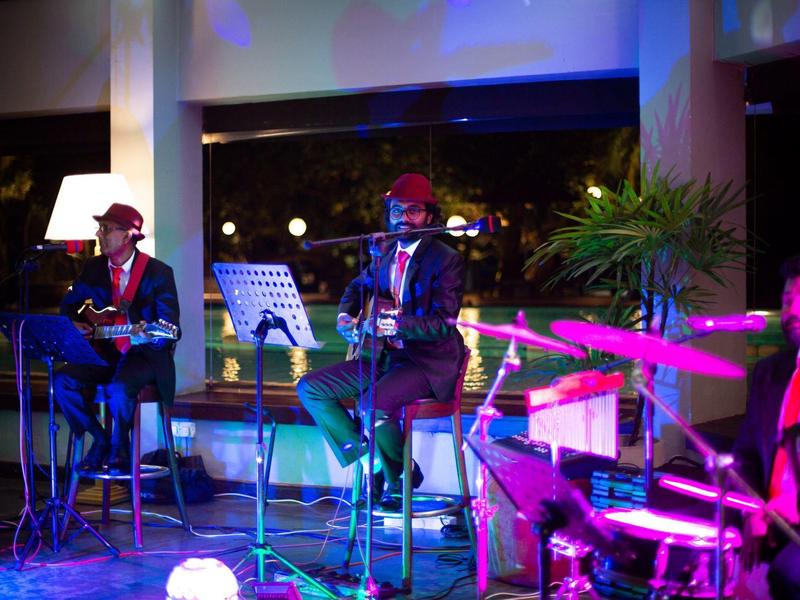 Drei Musiker spielen abends in farbig beleuchteter Bar, Gitarre, Keyboard und Schlagzeug sind zu sehen.