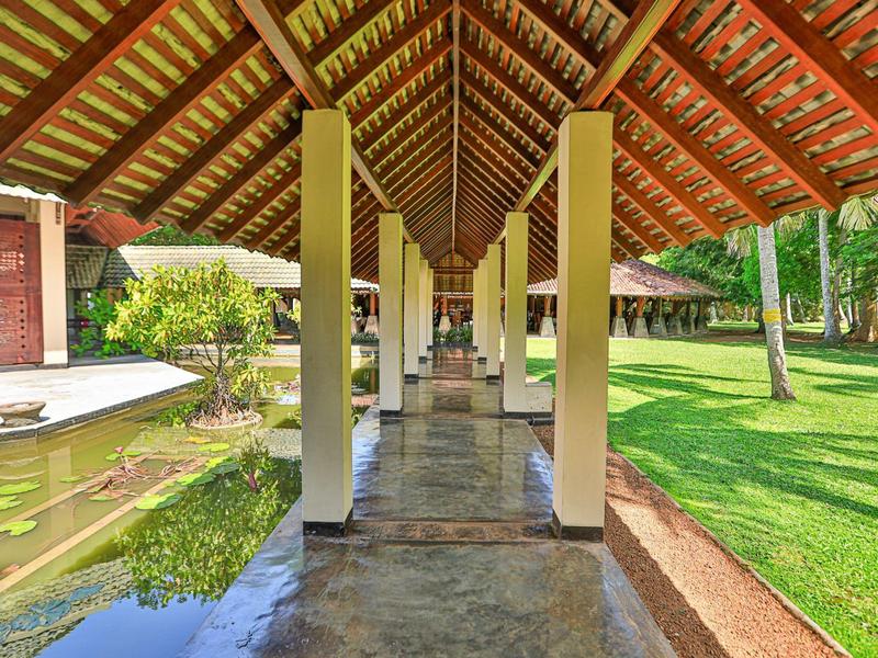 Überdachter Gang mit Holz- und Ziegeldach, Säulen, Wasserbecken links und grünem Rasen rechts.