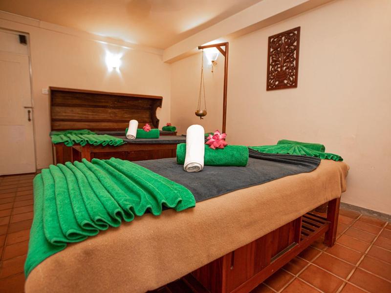 Behandlungsraum mit zwei Massageliegen, grünen Handtüchern und warmem, gedämpftem Licht.