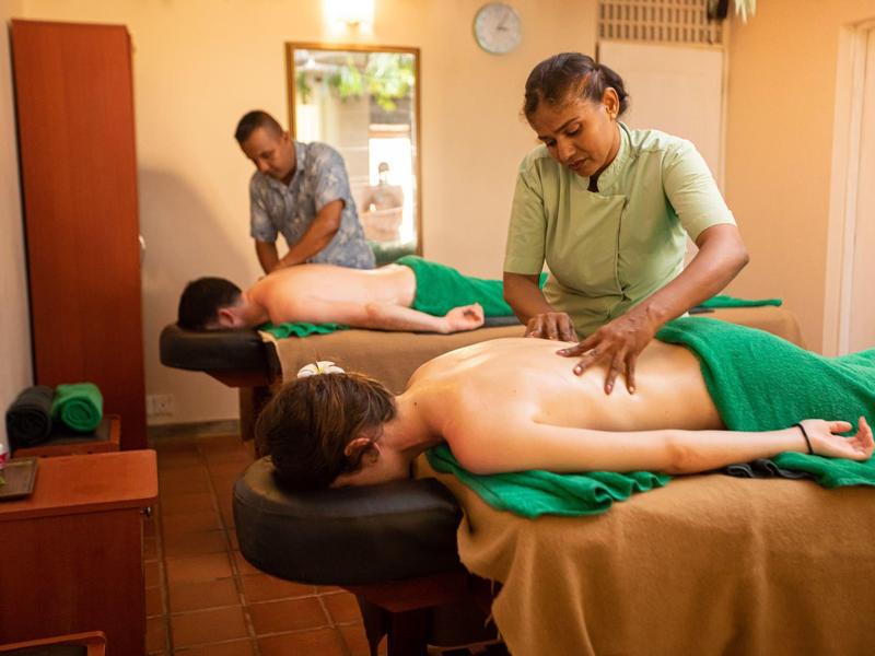 Zwei Personen erhalten Rückenmassagen in hellem Raum mit Holzmöbeln und warmem Licht.