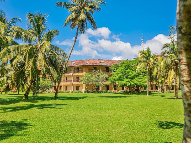 Ein großes Haus umgeben von Palmen und grünem Rasen unter blauem Himmel mit Wolken.