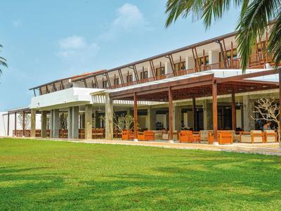 Modern hotel complex with large terrace and well-maintained lawn under a blue sky.