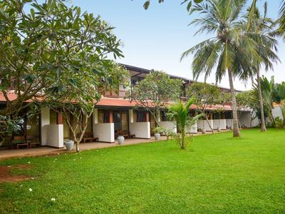 A long hotel building with a porch surrounded by green lawn and palm trees.