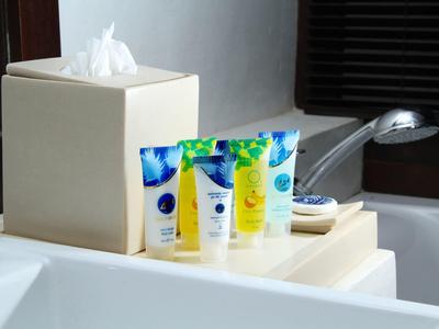 Hotel bathroom with tissue box and small toiletries on a shelf beside the bathtub.