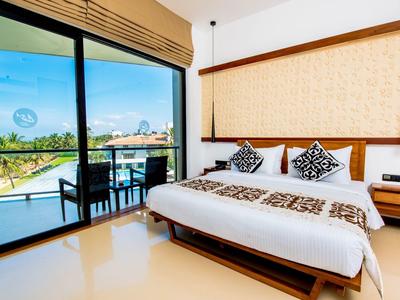Bright hotel room with large bed and balcony overlooking pool and palm trees.