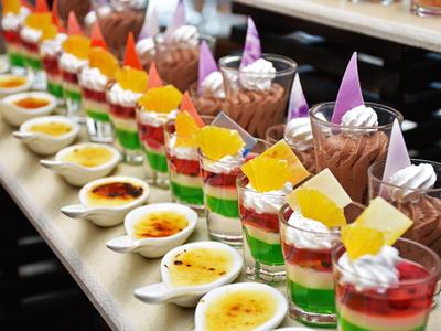 Row of colorful dessert glasses and creams on a white tray at a hotel buffet.