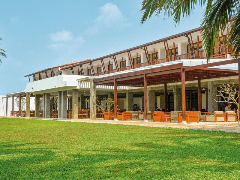 Modern hotel complex with large terrace and well-maintained lawn under a blue sky.