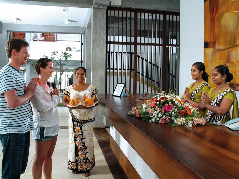 Two guests are welcomed by two staff members at the hotel reception.