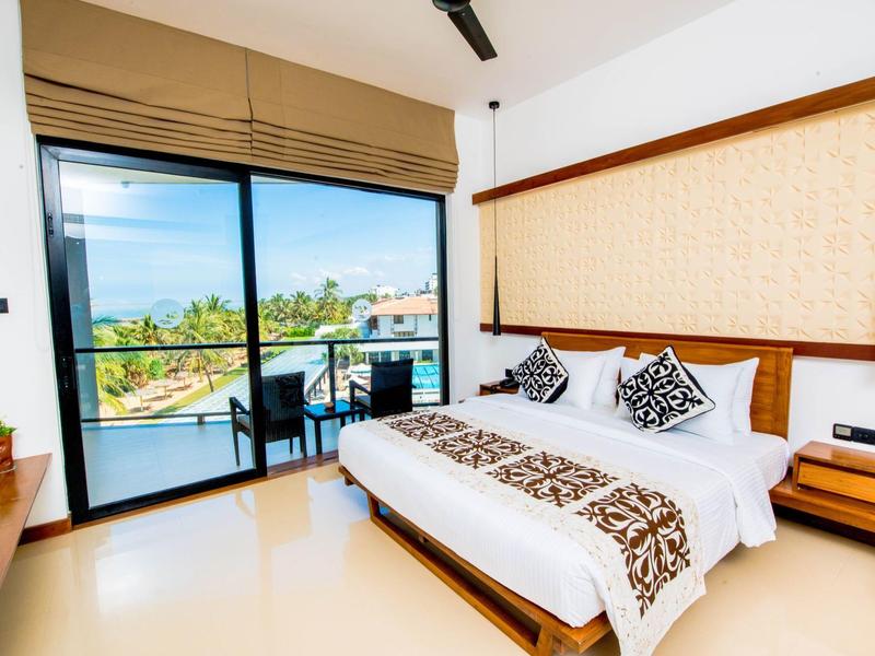 Modern hotel room with large bed and balcony overlooking the sea.