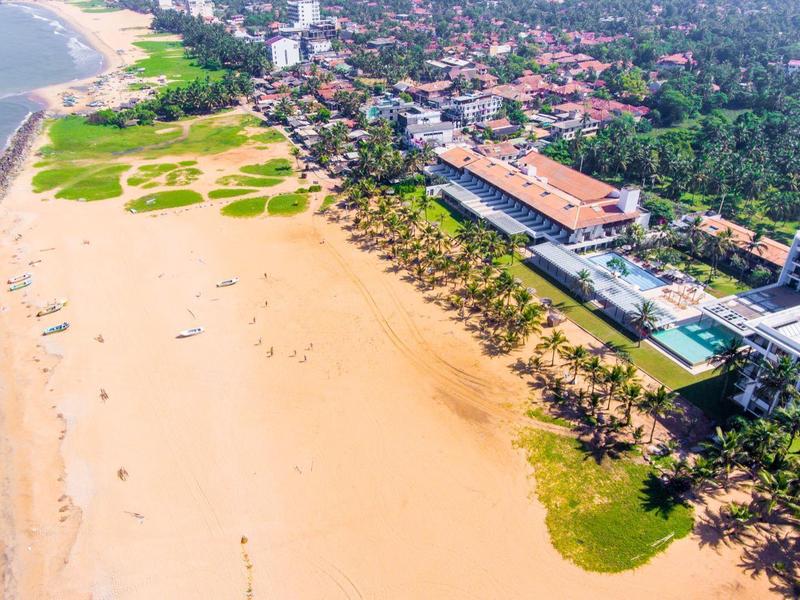 Aerial view of a hotel by the beach with a pool and adjacent sandy shore.