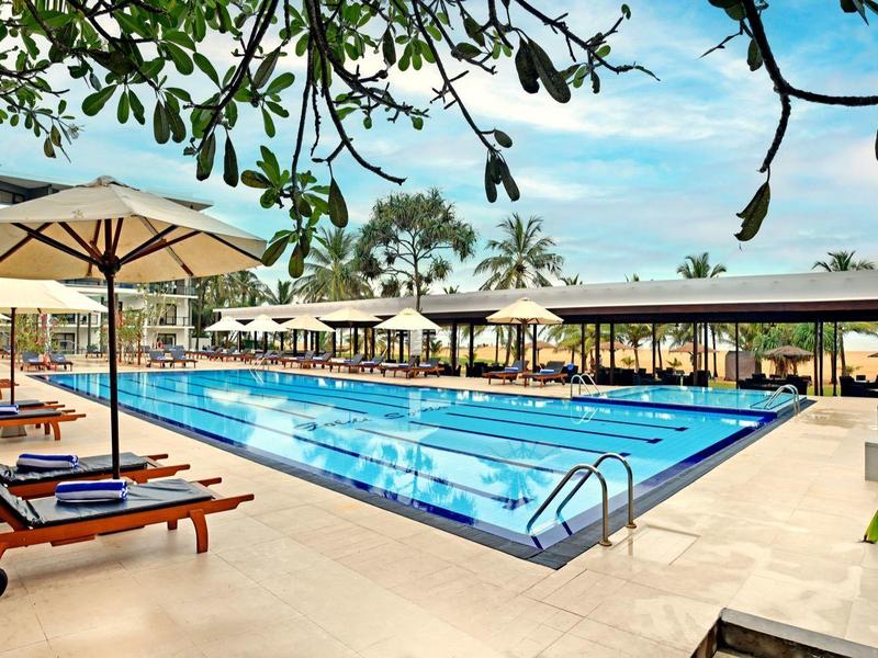 Modern hotel pool with lounge chairs and umbrellas under a blue sky.