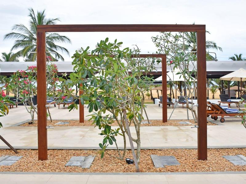 Outdoor area with wooden framed plants and lounge chairs on sandy beach near palm trees.