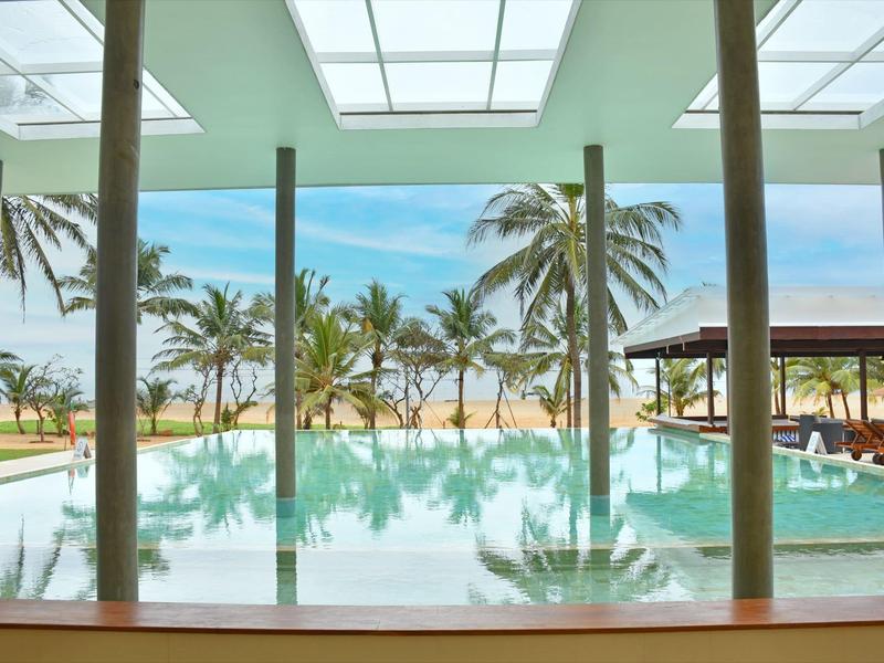 View through window of pool with palm trees and beach in the background.