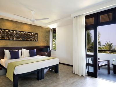 Modernes Hotelzimmer mit Balkon und Blick auf tropische Pflanzen bei Sonnenuntergang.