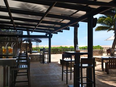 Überdachte Terrasse mit Bar und Sitzgelegenheiten in einem tropischen Hotel mit Blick auf den Strand.
