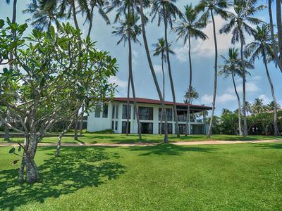 Ein modernes Haus mit Glasfront umgeben von Palmen und grünem Rasen unter blauem Himmel.