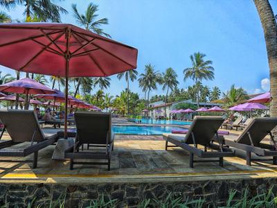 Poolbereich mit Liegestühlen und bunten Sonnenschirmen unter Palmen bei klarem Himmel.