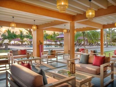 Offener Lounge-Bereich mit Holzmöbeln und Kissen, Blick auf Palmen und Pool.