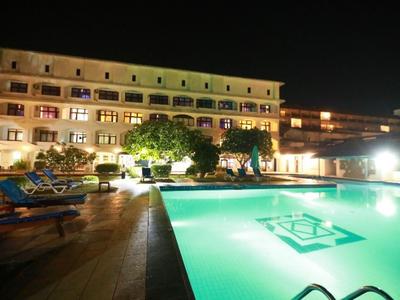 Beleuchteter Hotelpool mit Liegestühlen bei Nacht und mehrstöckigem Gebäude im Hintergrund.