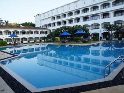 Großes Schwimmbad vor einem weißen Hotelgebäude mit blauen Sonnenschirmen.