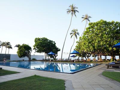 Swimmingpools mit blauen Sonnenschirmen und Palmen bei klarem Himmel in einem Hotelresort.