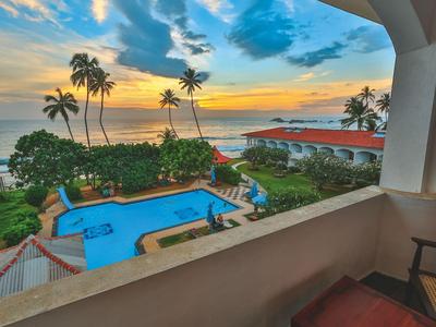 Blick von einem Balkon auf einen Pool, Palmen und den Ozean bei Sonnenuntergang.