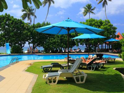 Hotelpool mit Liegestühlen und blauen Sonnenschirmen an tropischem Himmel und Palmen.