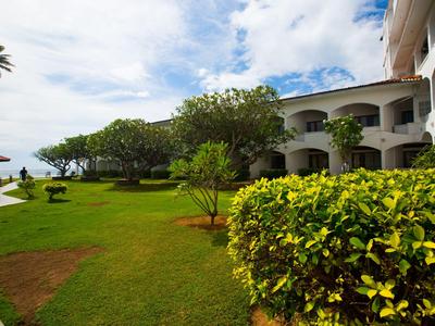 Hotel mit großzügigem, gepflegtem Garten und Blick aufs Meer bei bewölktem Himmel.