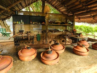 Rustic covered outdoor cooking area with pots on the ground and wooden stools