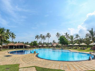 Large pool with sun umbrellas and palm trees in tropical resort under blue sky