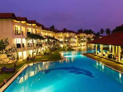 Ein beleuchteter Pool neben einem Hotelgebäude bei Dämmerung mit reflektierendem Wasser.