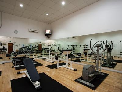 Fitnessraum mit verschiedenen Trainingsgeräten, Spiegelwand und Holzboden.