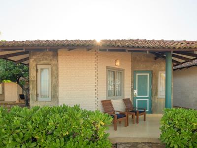 Small vacation house with green door, two chairs on the porch, and green bushes in front.