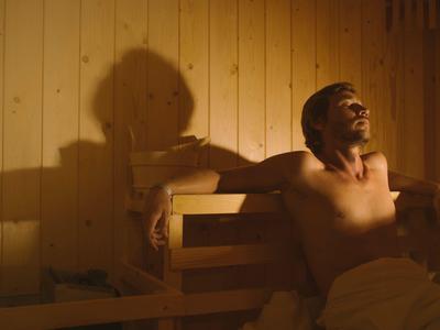 A man relaxes in a sauna with wooden paneling and warm lighting.