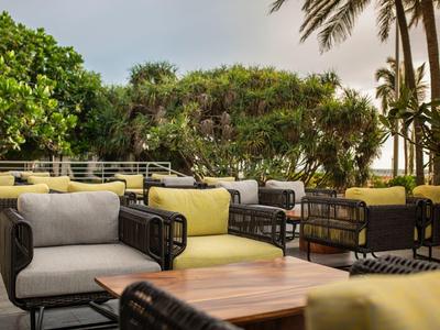 Cozy outdoor lounge with armchairs, tables, and palm trees in a tropical setting.