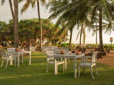 Mehrere gedeckte Tische mit weißen Stühlen auf einer Rasenfläche unter Palmen.
