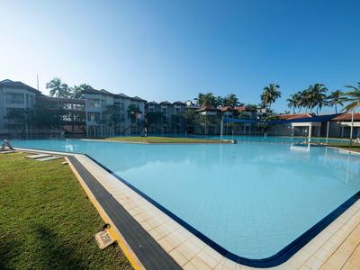 Large clear swimming pool surrounded by buildings and palm trees under a clear sky.
