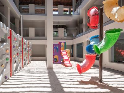 Bright, modern indoor courtyard playground with climbing wall and colorful play equipment.